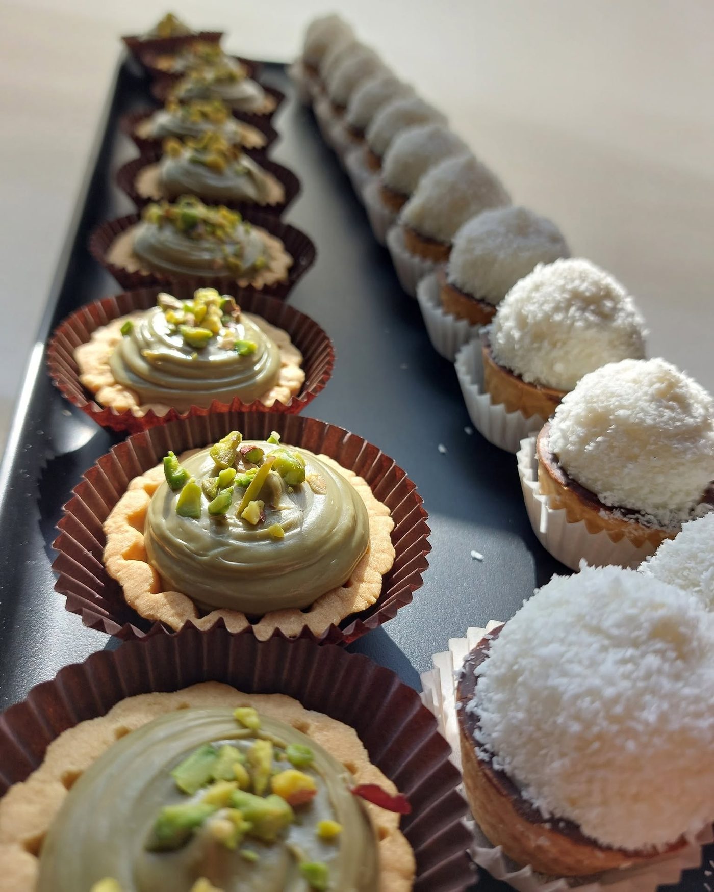 Tartellette alla crema di pistacchio e al cocco in fila sul vassoio
